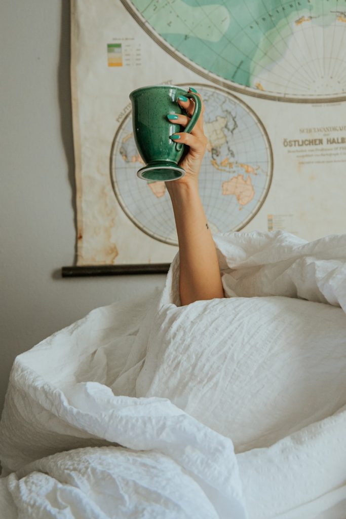 a person laying in bed with a cup in their hand